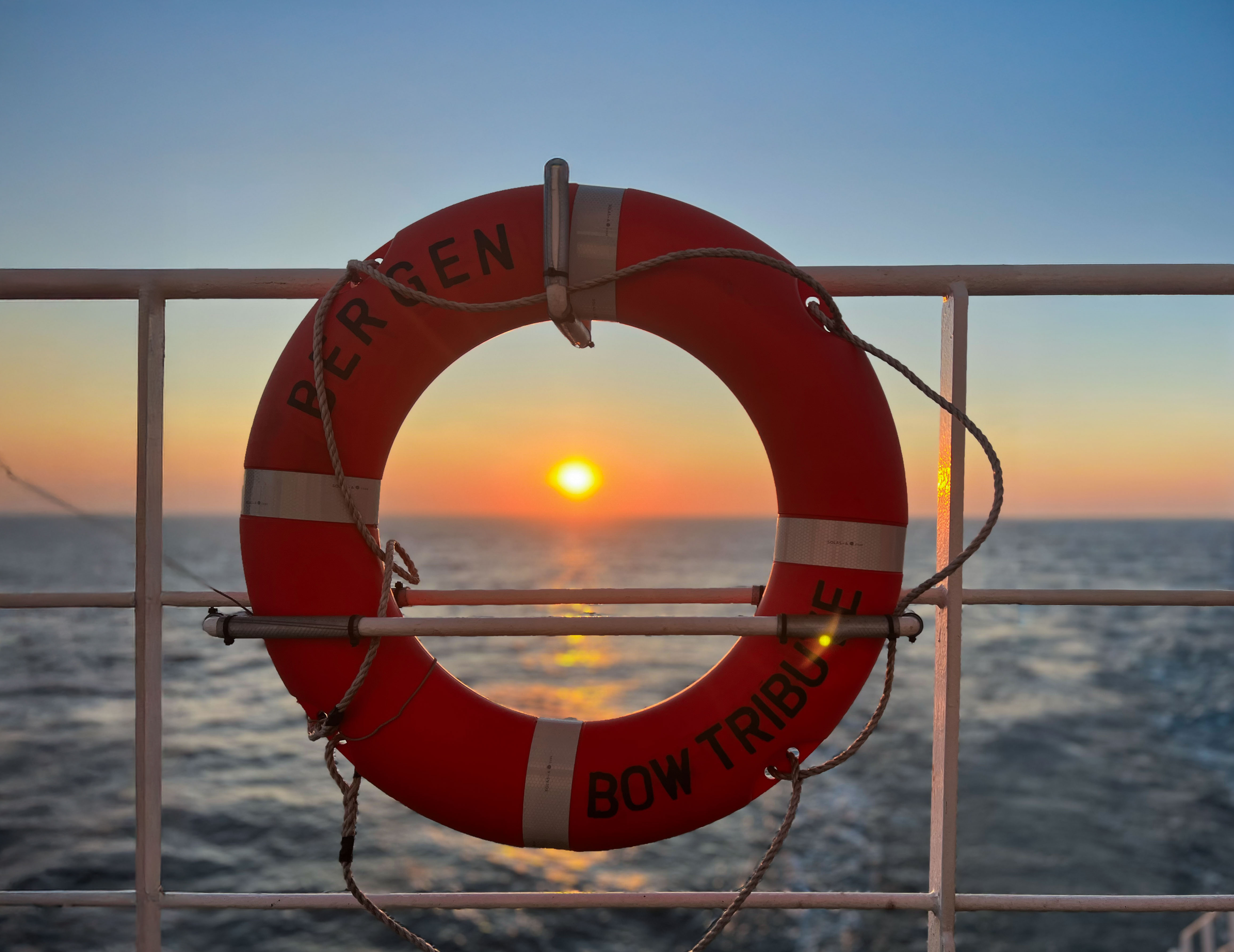Odfjell lifebuoy on ship deck framing sunset over calm ocean.