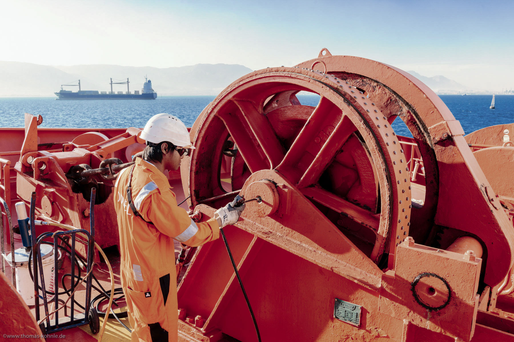 Odfjell crew member operating winch system on chemical tanker with cargo ship in background.