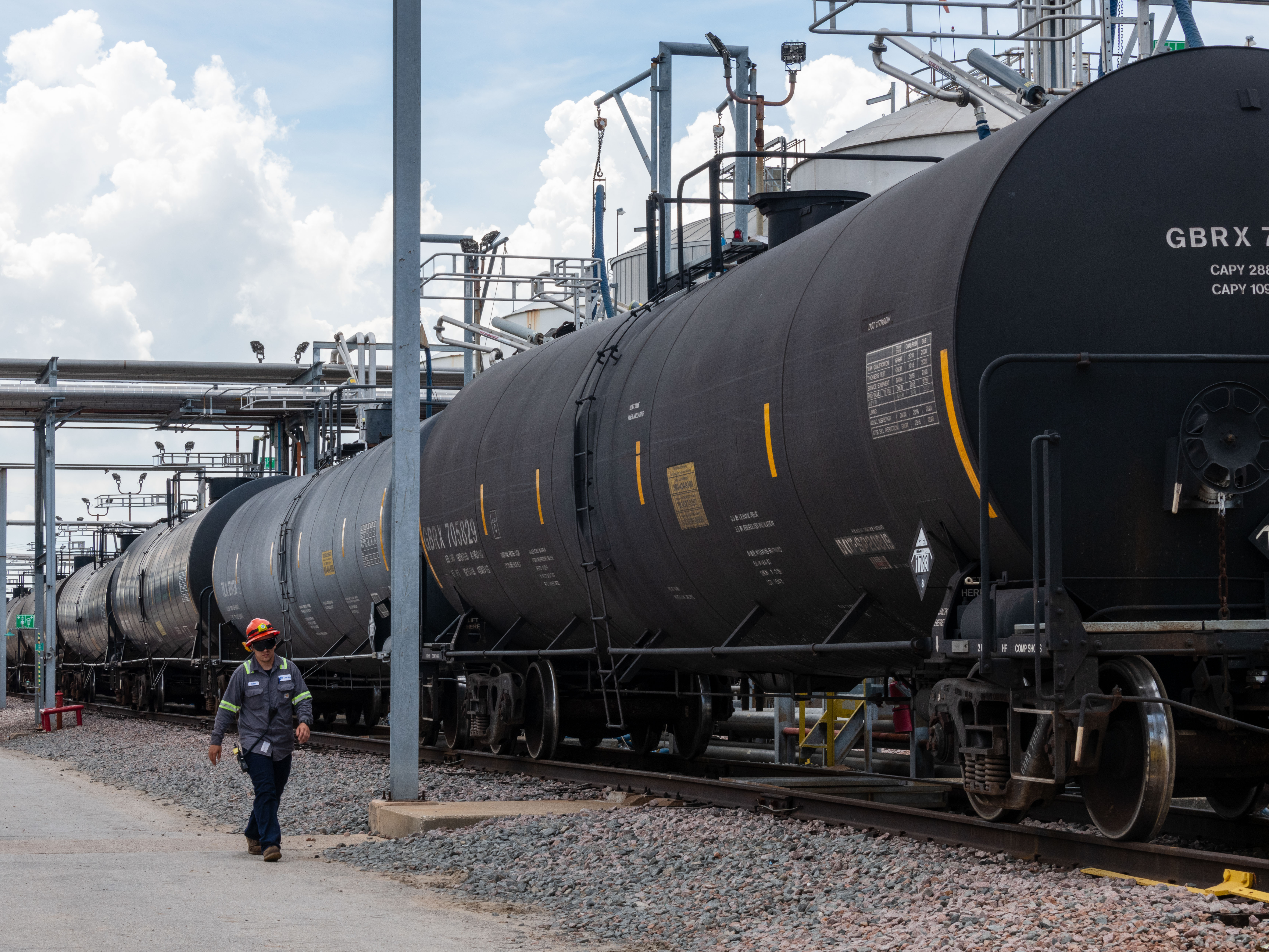 Odfjell terminal operator inspecting a line of rail tank cars under blue sky.