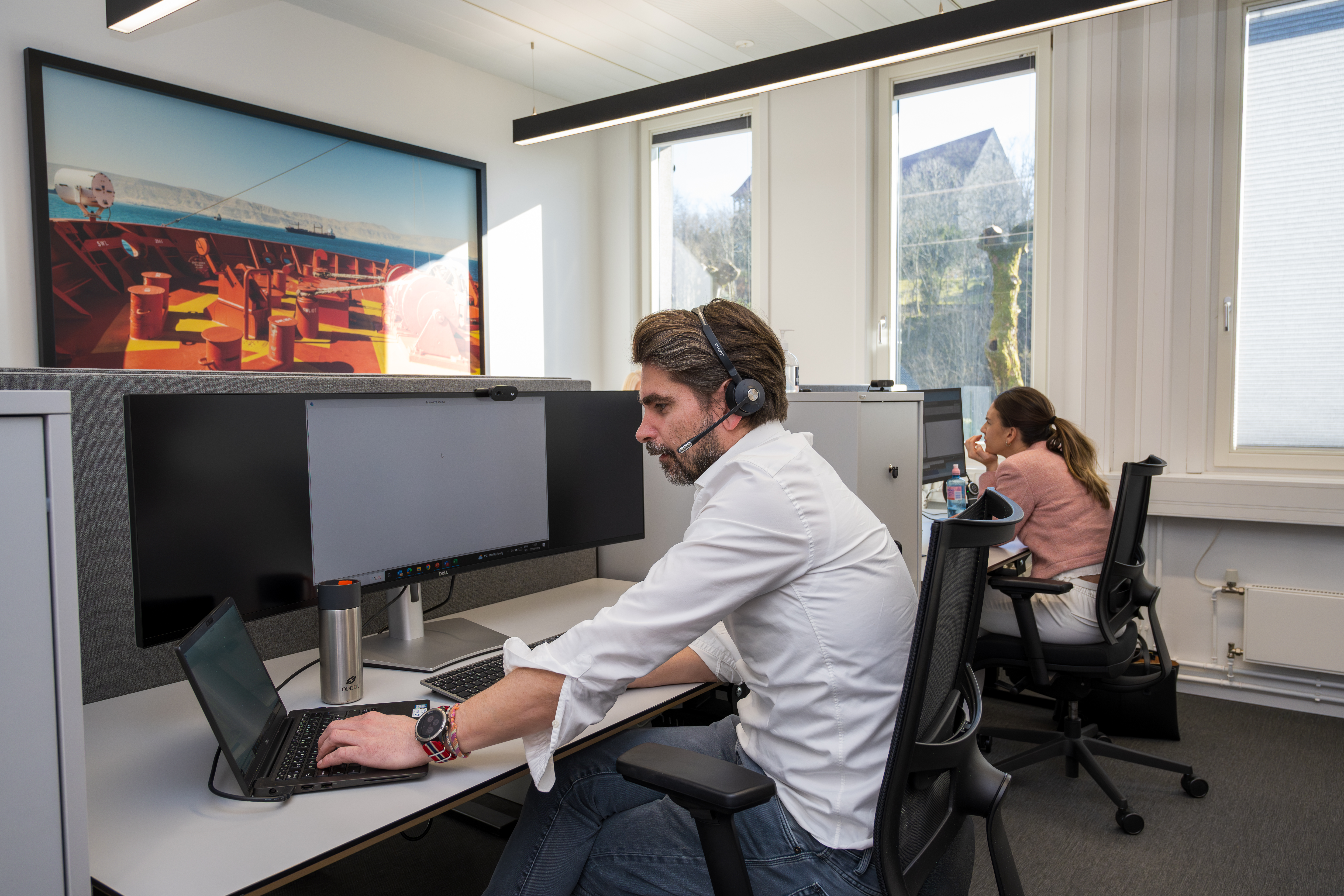 The Head of Corporate Tax is in a call, working from a modern office workstation while coordinating with colleagues nearby.