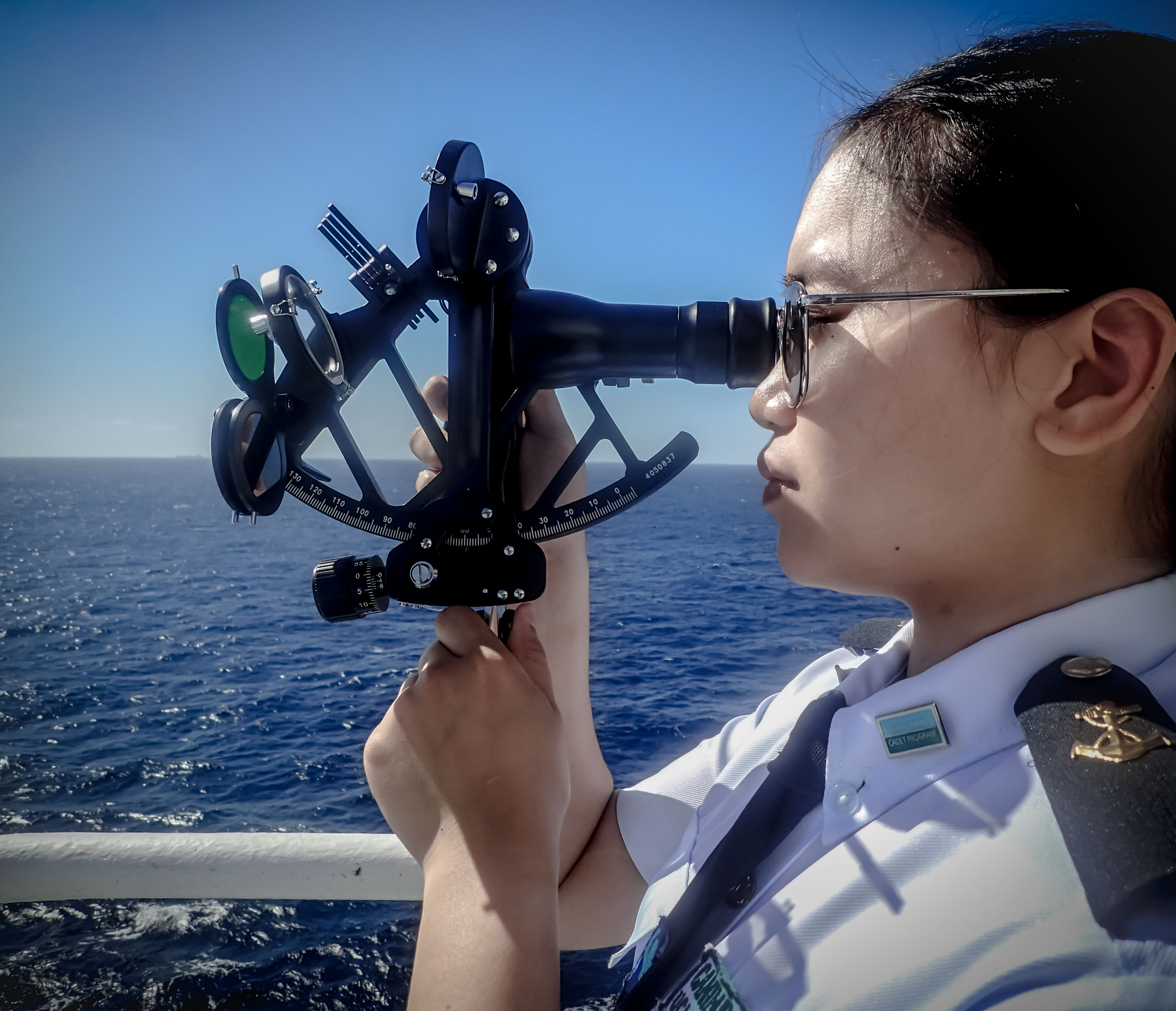 Odfjell cadet using a sextant for celestial navigation on open sea under clear blue sky.