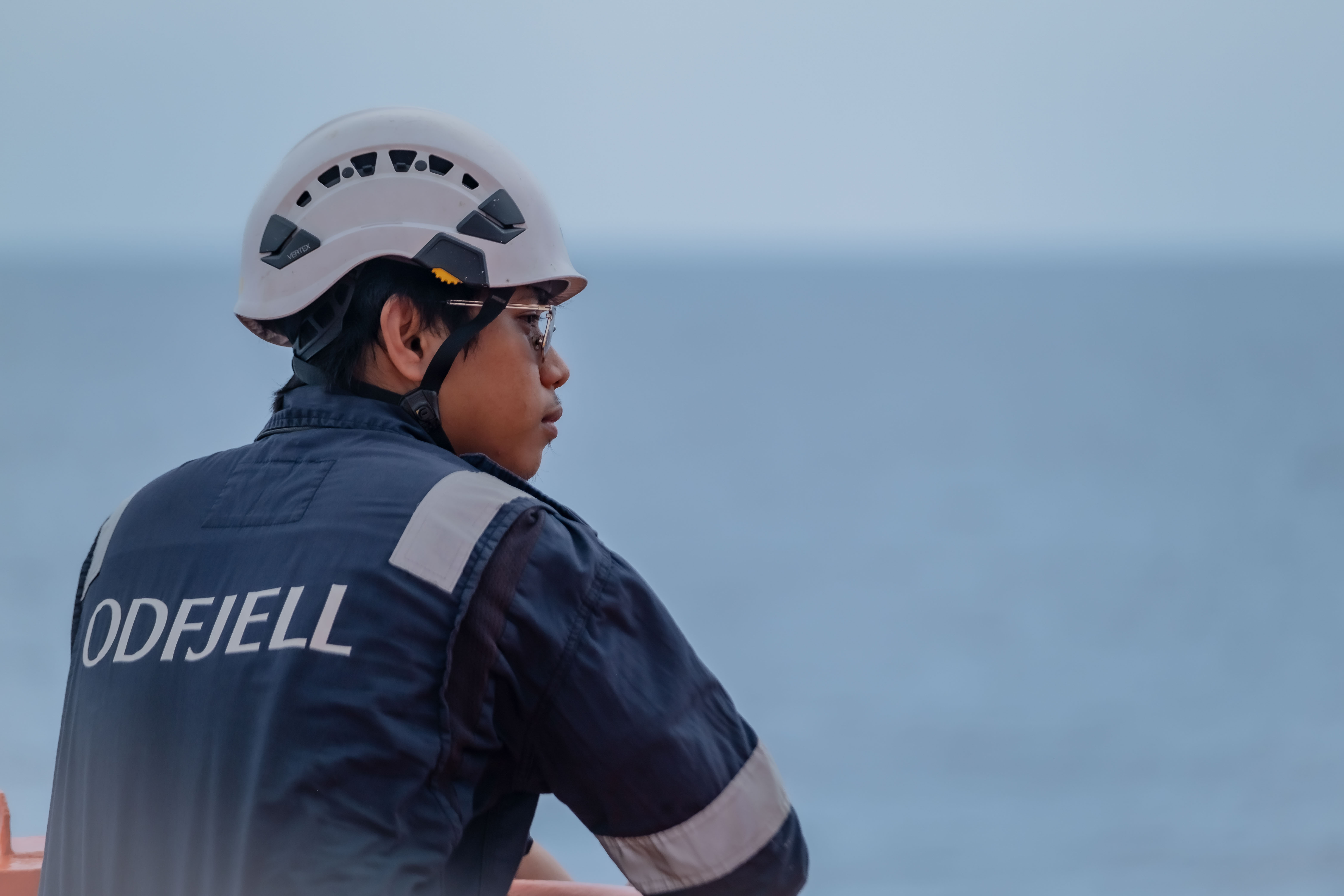 Odfjell crew member in blue uniform and helmet standing on deck and looking out to sea.