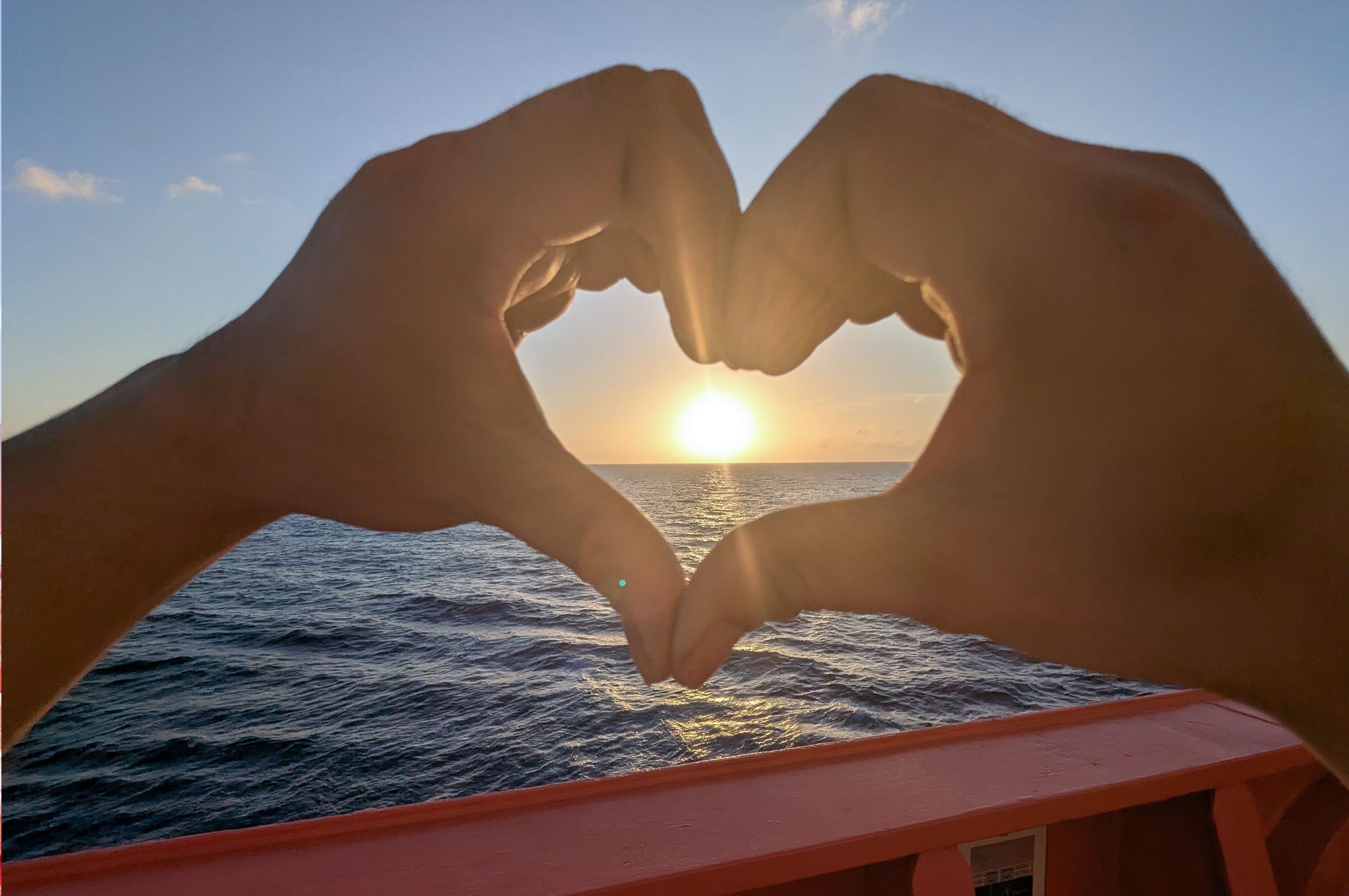 Hands forming a heart shape at sunset aboard an Odfjell tanker, symbolizing passion for life at sea.