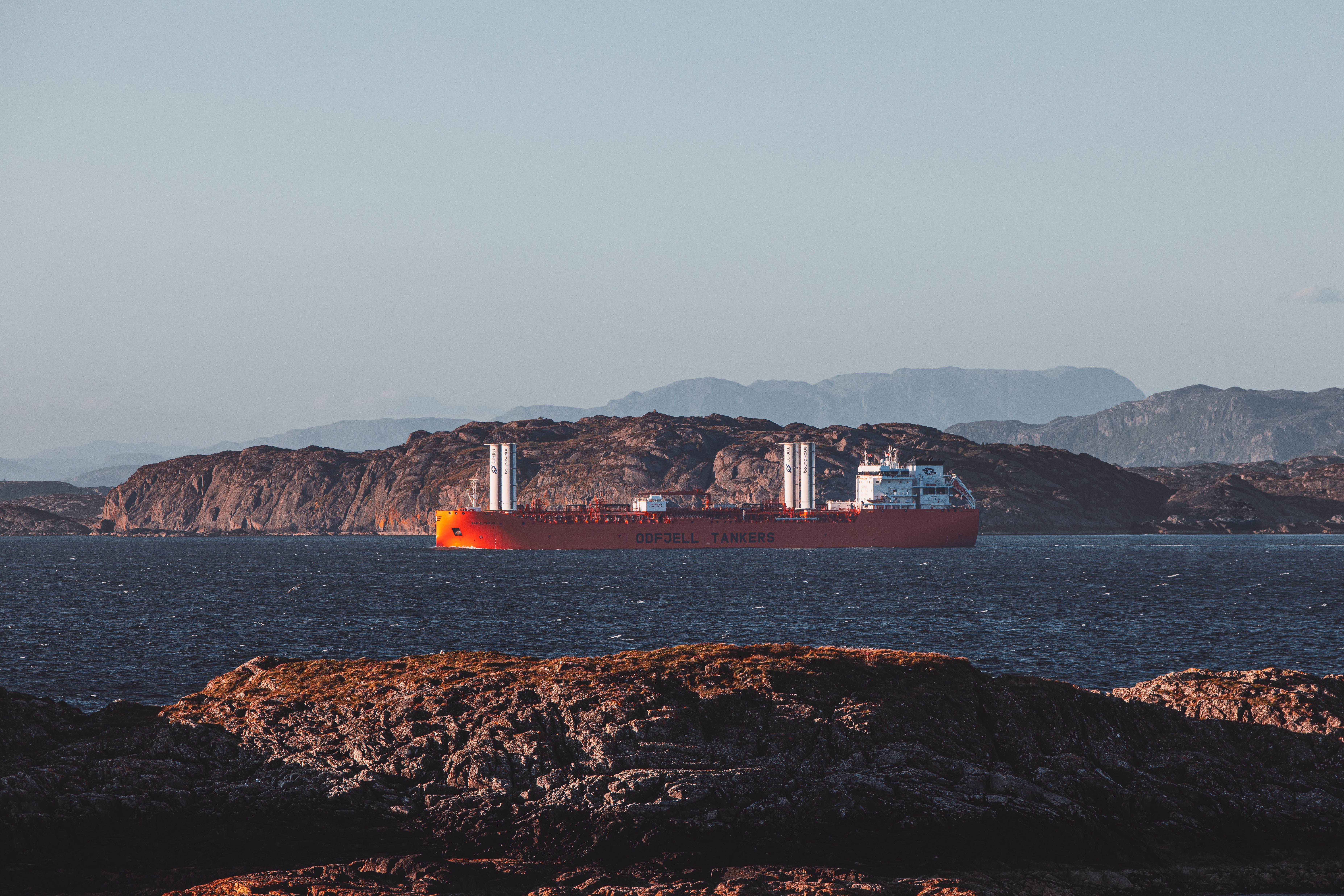Odfjell Tankers vessel with rotor sails sailing along the Norwegian coast, with rocky shoreline and mountains in the background.