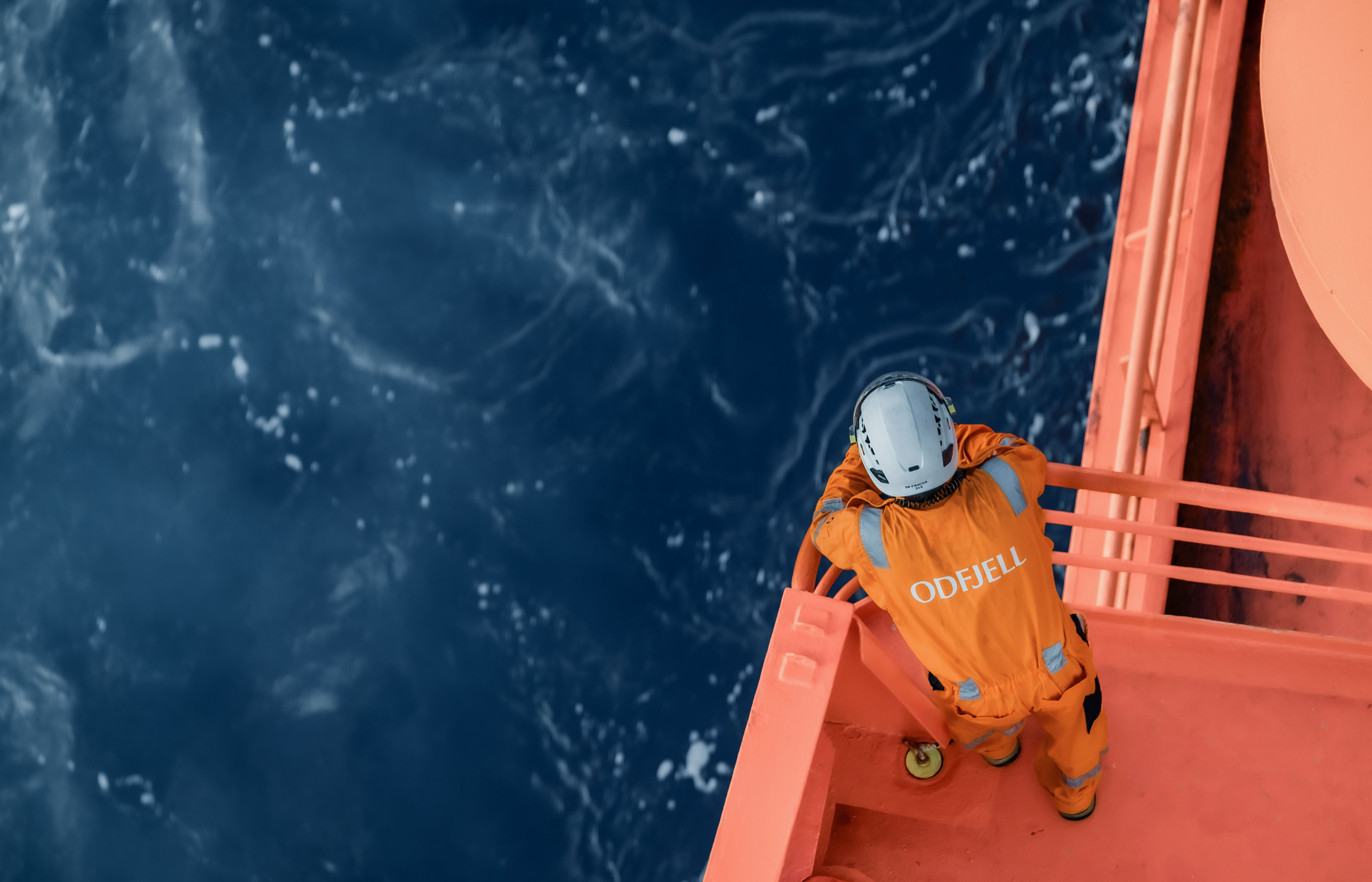 Odfjell crew member in orange uniform standing on deck overlooking the ocean.