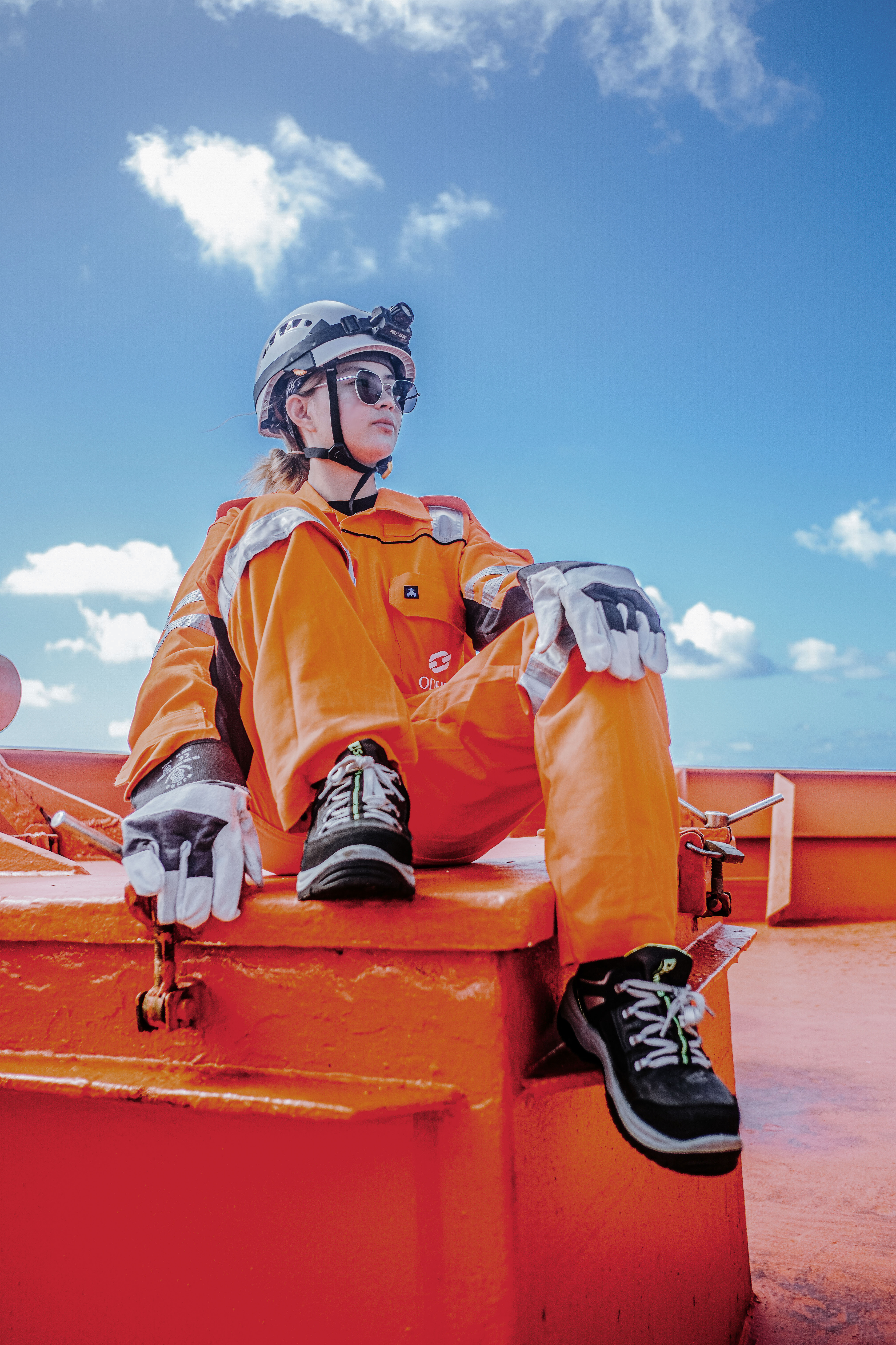 Odfjell seafarer sitting on deck in safety gear under clear blue sky.