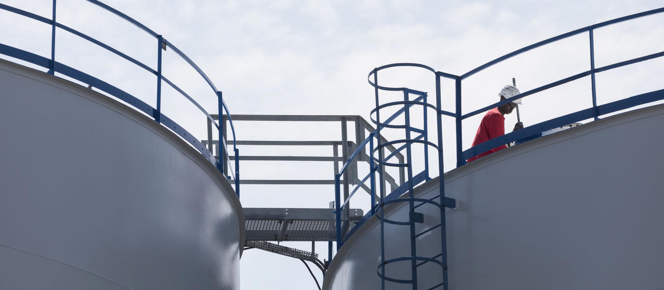 Odfjell terminal worker inspecting a chemical storage tank under bright sky.