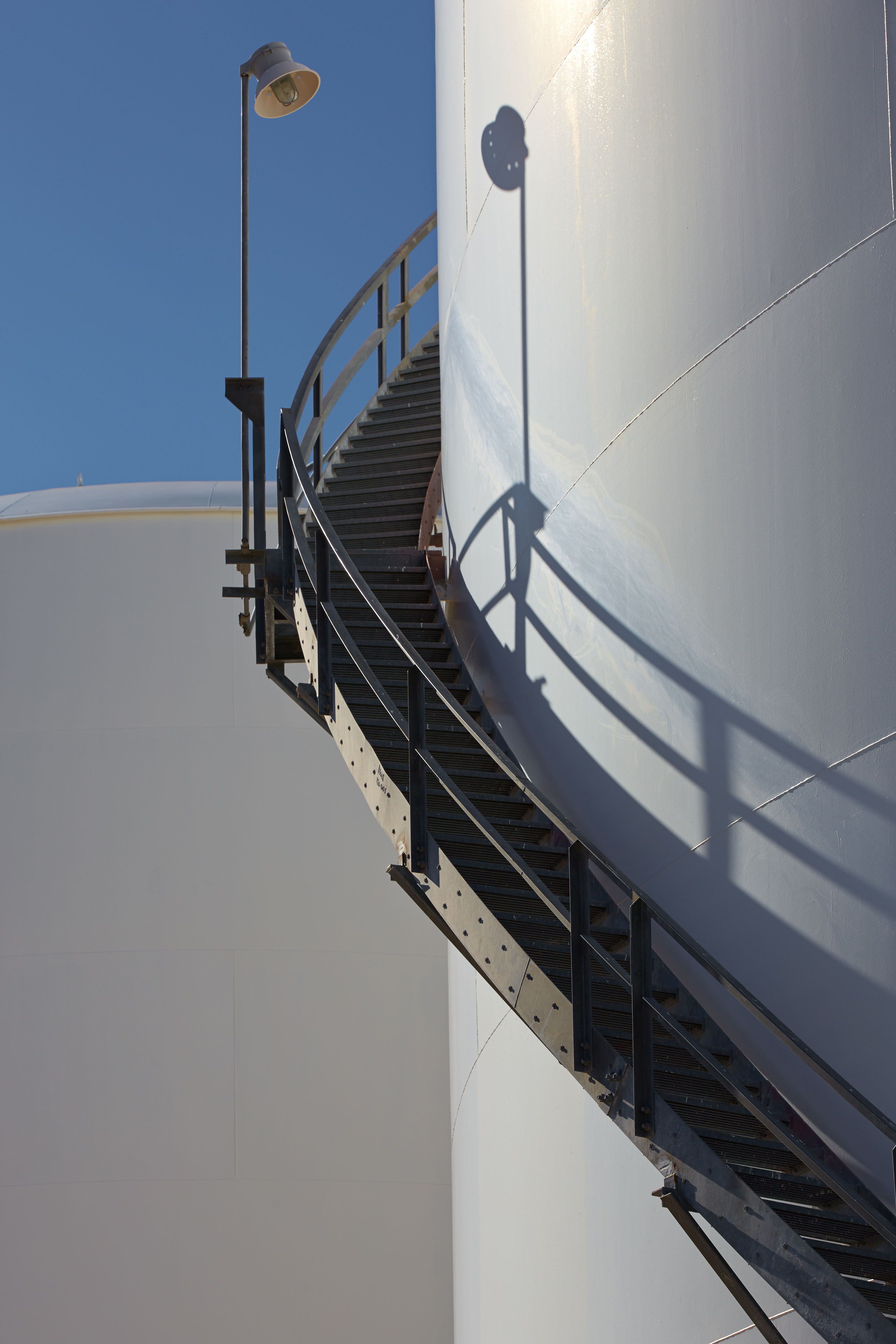 Industrial staircase and shadow detail on Odfjell storage tank under bright sunlight.
