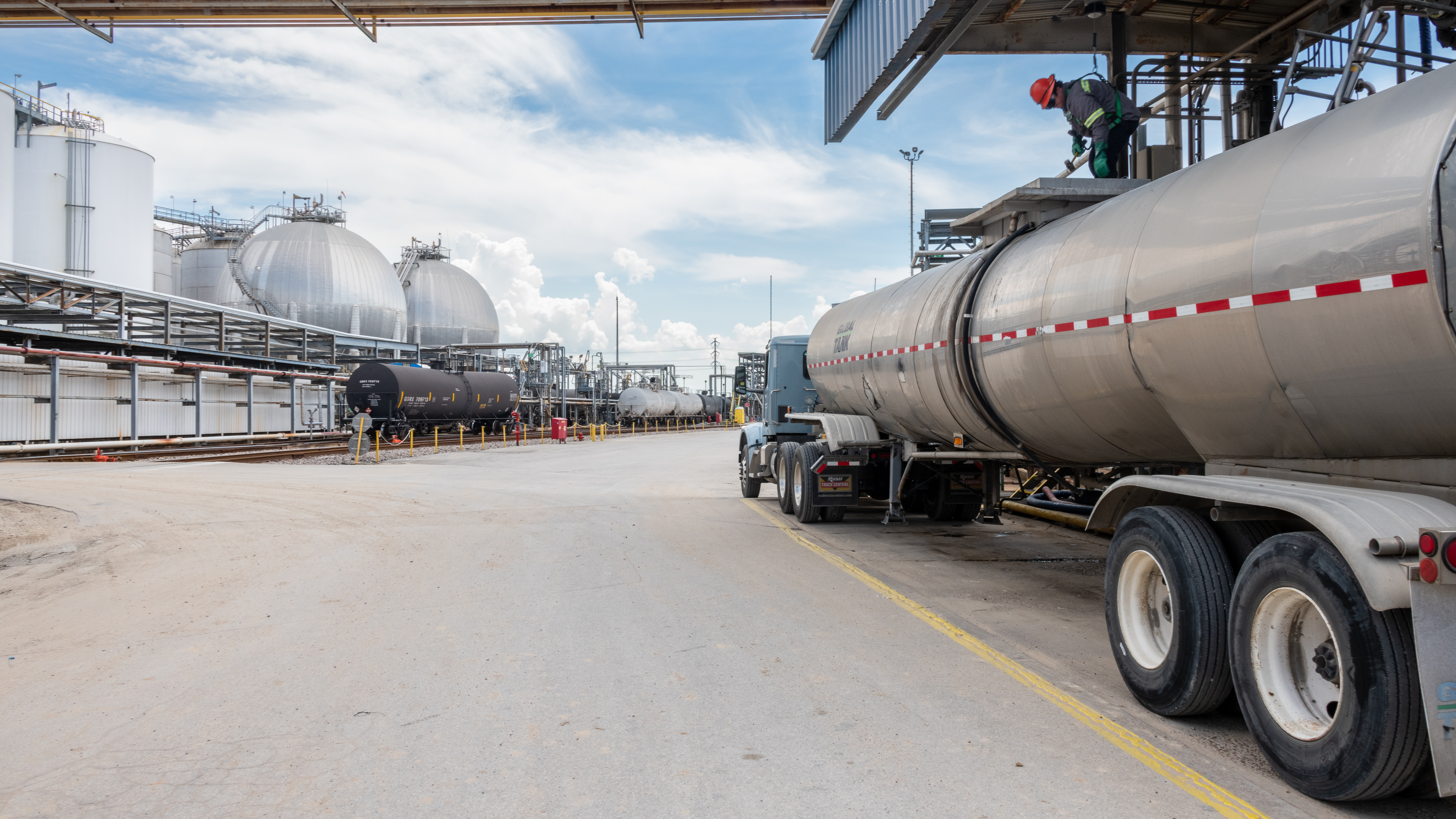 Worker loading chemical tank truck at Odfjell terminal with spherical storage tanks in the background.
