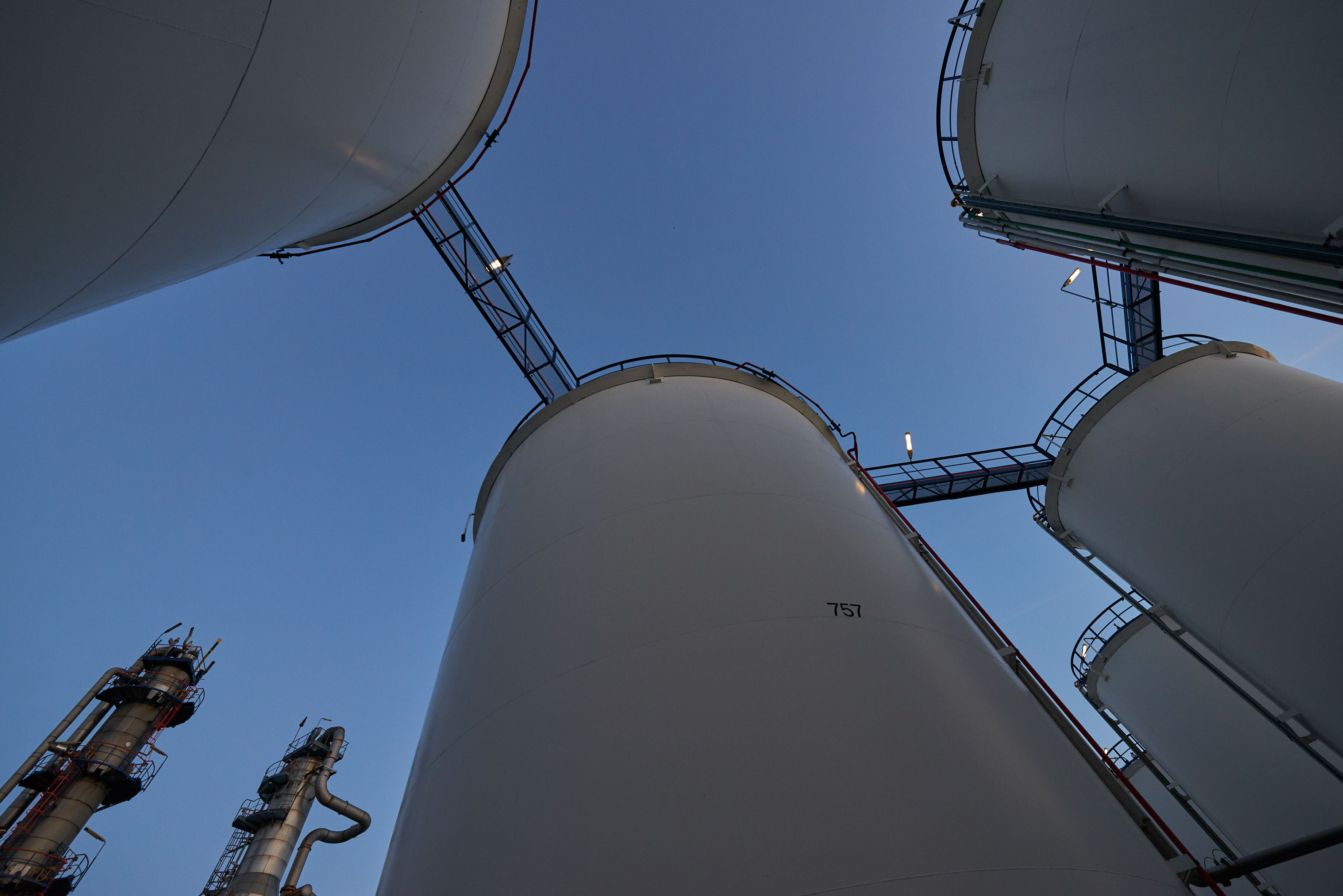 Low-angle view of Odfjell terminal storage tanks and connecting pipes under clear blue sky.