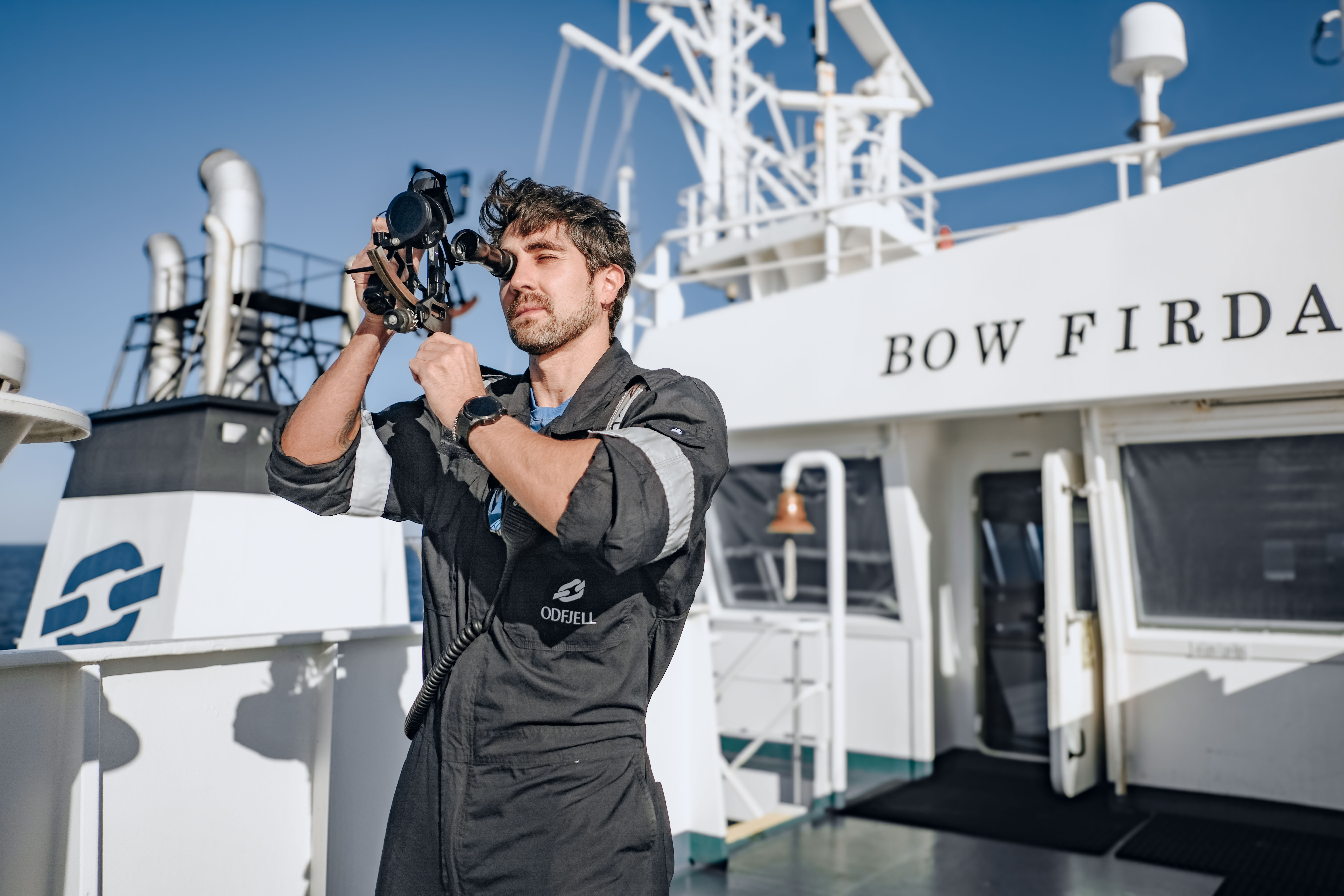 Odfjell crew member on board Bow Firda using a sextant for navigation under clear blue sky.