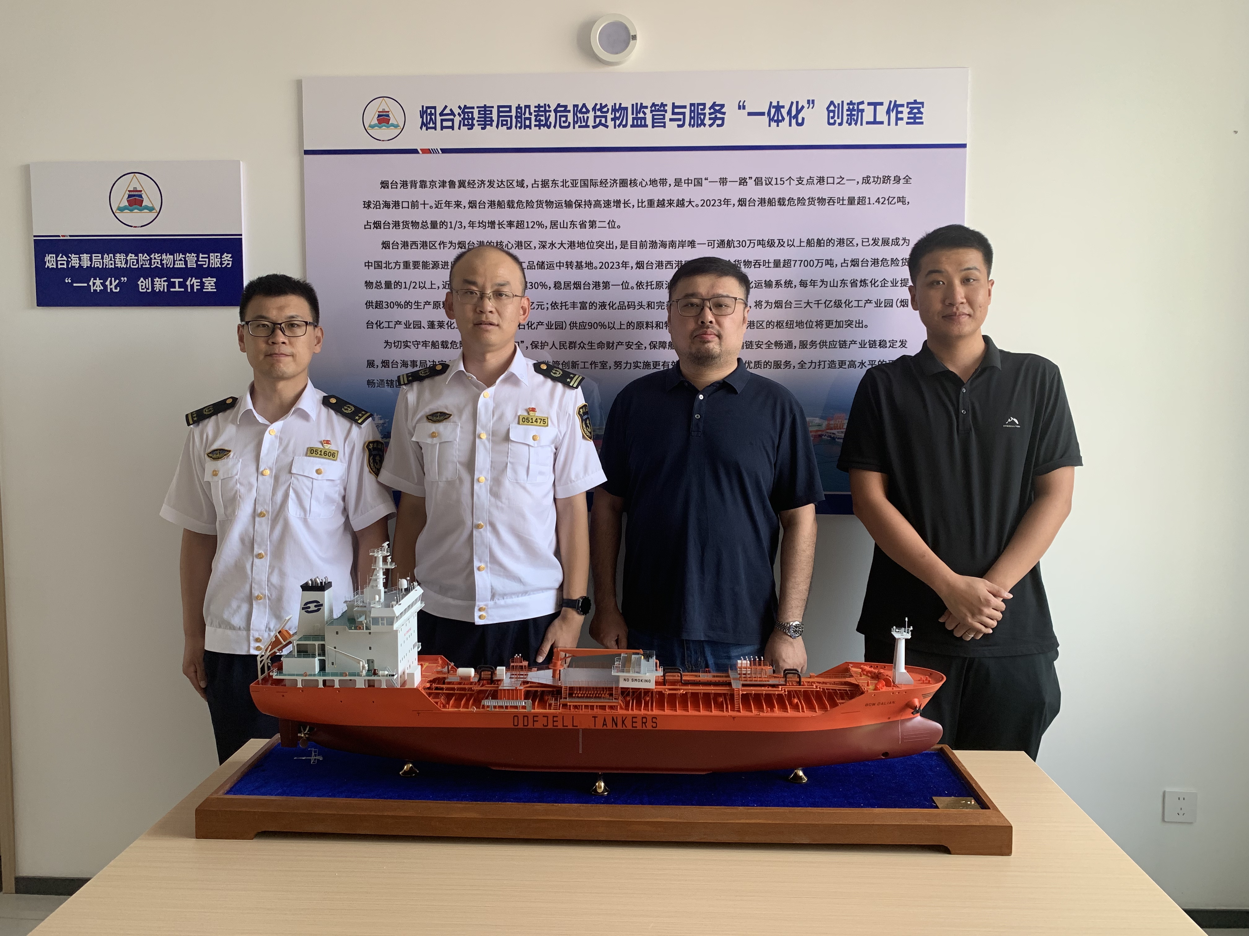 Showing four people with a model of a boat in front.