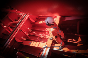 Odfjell crew member in orange uniform standing inside the ship structure performing inspection work.