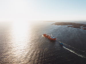 Aerial view of Odfjell chemical tanker with rotor sails being guided by a tugboat through coastal waters at sunset.