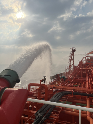 Safety exercise aboard an Odfjell tanker using a foam cannon system under bright sunlight at sea.