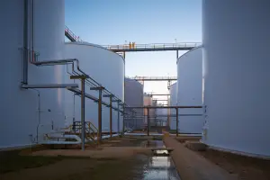 Two workers standing on walkway between large white chemical storage tanks at Odfjell terminal.