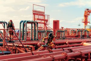 Crew working on deck surrounded by red pipelines and valves, wearing safety harnesses and protective gear.