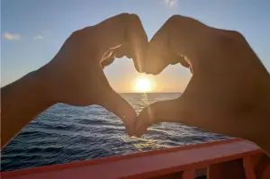 Hands forming a heart shape at sunset aboard an Odfjell tanker, symbolizing passion for life at sea.